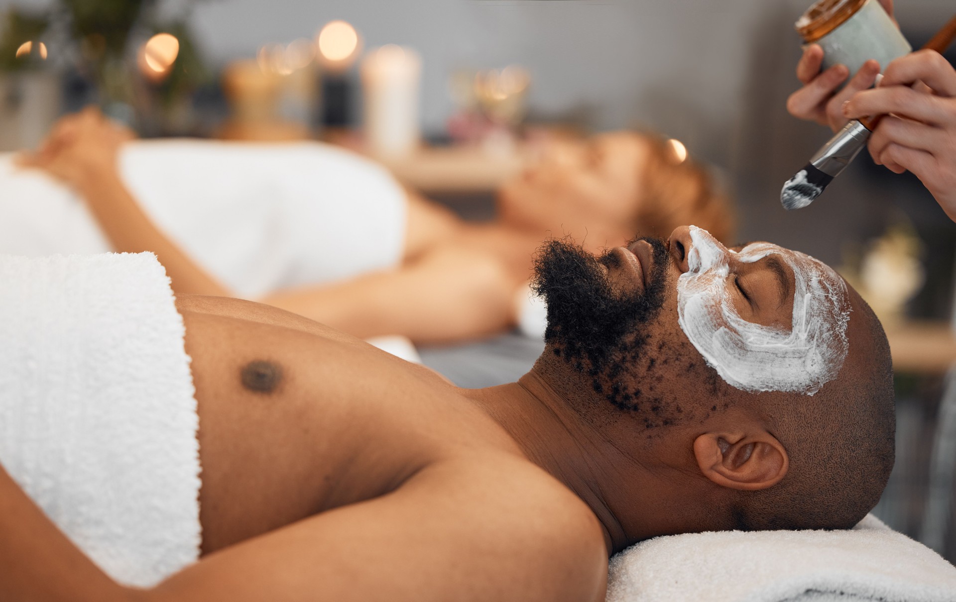 Skincare, wellness and black man getting a facial at a spa for relaxation, calm and satisfaction. Beauty, luxury treatment and couple massage at beauty salon together, skincare products on man's face Skincare, wellness and black man getting a facial at a spa for relaxation, calm and satisfaction. Beauty, luxury treatment and couple massage at beauty salon together, skincare products on man's face
